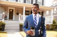 business man with coffee in front of house to represent insurance 101 for landlords_NREIG