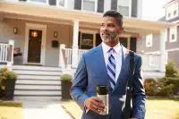 business man with coffee in front of house to represent insurance 101 for landlords_NREIG