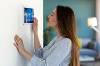 Woman adjusting a smart home thermostat panel, one of several ways to save energy at your rental.
