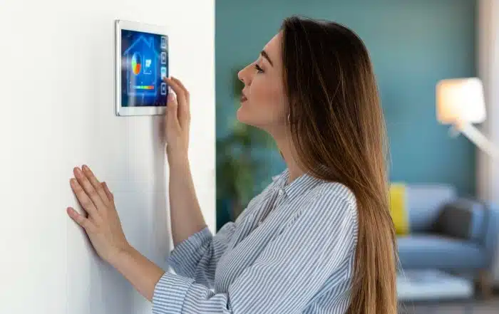 Woman adjusting a smart home thermostat panel, one of several ways to save energy at your rental.